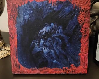 May include: Square canvas art featuring a dark, surreal scene. The artwork depicts a cluster of blue figures with outstretched hands against a dark blue and starry background. The canvas is framed with a textured red border, creating a striking contrast.