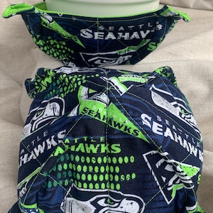 May include: A pair of blue and green fabric bowl cozies with a Seattle Seahawks logo and the words "Seattle Seahawks" printed on them.