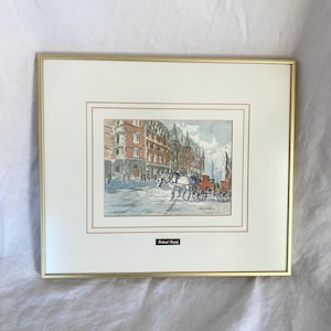 May include: Framed watercolor painting depicting a European street scene with buildings, a horse-drawn carriage, and pedestrians. The artwork is in a gold frame with a white mat. The artist's name, Roland Duire, is printed on a small black label.