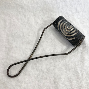 May include: A black and white patterned roller with a metal handle. The roller is used for creating patterns on surfaces.