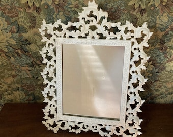 May include: White ornate picture frame with a decorative, scrolled design. The frame has a mirror inside.