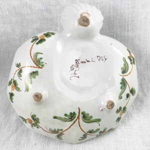 May include: White ceramic dish with green and gold floral designs. The bottom of the dish has three feet and a handwritten inscription that reads "ma fa ti, Italy".