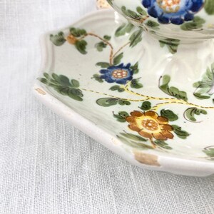 May include: A white ceramic pedestal bowl with a floral design. The bowl has a scalloped edge and features blue, yellow, and green flowers.