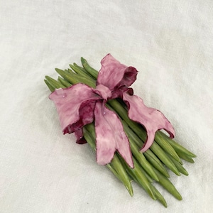 May include: A bouquet of green ceramic asparagus stalks tied together with a large pink ribbon.