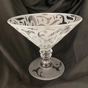 Puede incluir: Una copa de martini de cristal transparente con un diseño esmerilado y grabado. El cuenco de la copa tiene forma acampanada con un diseño decorativo. El tallo es corto y la base es redonda con un diseño grabado a juego. La copa se utiliza para cócteles.