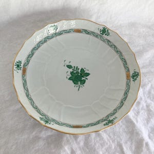 May include: A white porcelain serving bowl with a green and gold floral pattern. The bowl has a scalloped edge and a raised center.