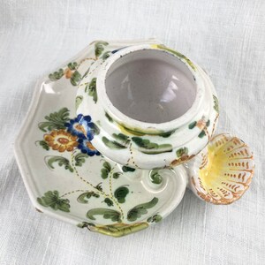 May include: A white ceramic dish with a floral design in shades of blue, yellow, and green. The dish has a raised edge and a scalloped handle. The dish is decorated with a floral pattern in shades of blue, yellow, and green.