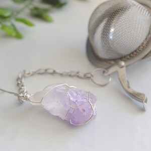 May include: A purple amethyst crystal wrapped in silver wire, attached to a silver chain and a silver tea infuser.
