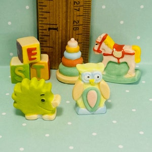 May include: A set of five miniature toys for a child's playroom. The toys include a rocking horse, a stack of colorful rings, a green hedgehog, a set of alphabet blocks that spell 'BEST', and a yellow and blue owl.