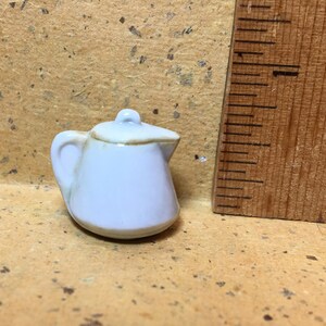 以下が含まれることがあります： 茶色の縁取りと蓋が付いた、小さな白い陶器製のティーポット。ティーポットの高さは約5センチメートルです。