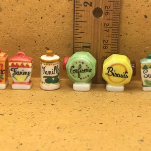 Puede incluir: Seis tarros de cerámica en miniatura con diseños coloridos y palabras francesas. Los tarros están etiquetados como "Cacao", "Farine", "Vanille", "Confiserie", "Biscuits" y "Sucre".