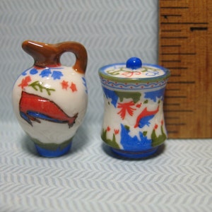 May include: Two miniature ceramic containers with blue, red, and green floral designs. The larger container has a lid and the smaller container is a pitcher.