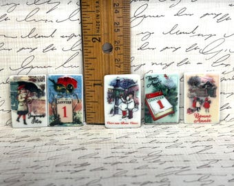 May include: Five rectangular ceramic tiles featuring vintage-style illustrations of winter scenes and the text 'Joyeuses Fetes', 'Janvier 1', 'Voici nos Bons Voeux', 'Bonne Annee', and 'Bonne Annee'. A wooden ruler shows the tiles are approximately 2.5 cm tall.