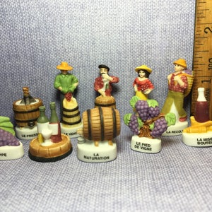 Może przedstawiać: Zestaw 10 miniaturowych ceramicznych figurek przedstawiających proces produkcji wina. Każda figurka przedstawia inny etap produkcji wina, od winogron po gotową butelkę. Figurki są pomalowane żywymi kolorami i mają szczegółowe cechy. Zestaw zawiera następujące etapy: La Grappe, Le Press, Le Vene, La Maturation, Le Pied de Vigne, La Recolt, La Mise en Bouteille.
