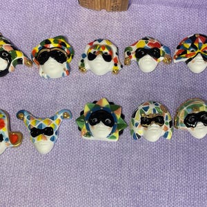 May include: Ten colorful ceramic masks with jester hats, each with a different design and color scheme. The masks have black eyes and are painted with intricate details.