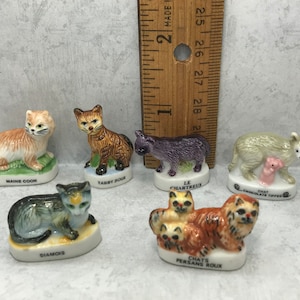 Puede incluir: Conjunto de seis figuritas de gato de cerámica en miniatura, cada una representando una raza diferente. Las figuritas están pintadas en colores realistas y presentan detalles como bigotes y pelaje. Las razas incluyen Maine Coon, Tabby Roux, Le Chartreux, Siamés, Chat Chocolate Tipped y Chats Persans Roux.