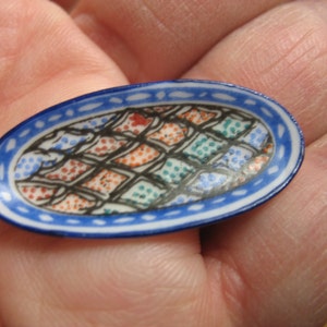 May include: A small, blue and white ceramic dish with a geometric pattern in shades of red, orange, green, and blue.
