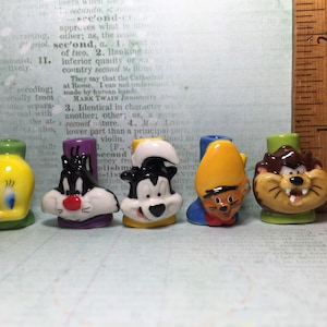 Puede incluir: Seis pequeñas figuritas de cerámica de personajes de dibujos animados. Los personajes son Piolín, Silvestre el gato, Bugs Bunny, el Pato Lucas y el Demonio de Tasmania. Las figuritas están pintadas en colores brillantes y tienen un estilo caprichoso.