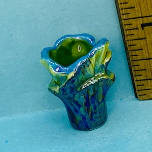 May include: A small, blue and green ceramic planter with a ruffled top. The planter has a mottled glaze with shades of blue, green, and yellow.