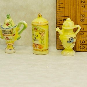 Puede incluir: Tres figuritas de cerámica en miniatura: una taza amarilla y verde con asa, una botella amarilla y dorada con una etiqueta que dice "Pilule de Studious", y una jarra amarilla con un diseño de pájaro azul.