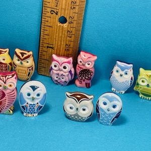 Op de afbeelding: Een verzameling van tien kleine keramische uilbeeldjes in verschillende kleuren en patronen. De uilen zijn allemaal ongeveer 2,5 cm hoog en hebben verschillende uitdrukkingen.