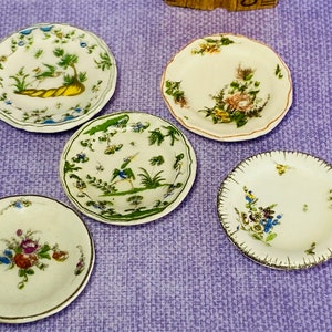 Puede incluir: Juego de cuatro platos decorativos pequeños con diseños florales y de pájaros. Los platos son blancos con detalles azules, verdes y amarillos.