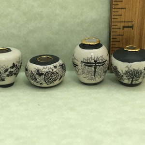 May include: Four small ceramic vases with black and white designs. The vases have a gold rim and are decorated with different patterns, including butterflies, leaves, and a dragonfly.