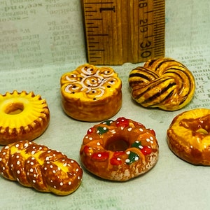 May include: Six miniature ceramic pastries in various shapes and colors, including a donut, a braided loaf, a swirl, and a ring with red and green icing.