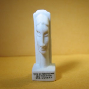 Puede incluir: Escultura de cerámica blanca de una cabeza de Amedeo Modigliani. La escultura está sobre una base blanca con el texto "TETE DE MODIGLIANI © PRESTIGE DES MUSEES".