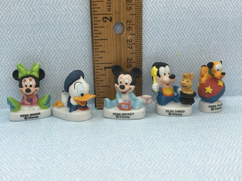 Może przedstawiać: Zestaw pięciu porcelanowych figurek postaci z Disneya, w tym Myszki Miki, Minnie Mouse, Kaczora Donalda, Goofy'ego i Pluto. Każda figurka ma około 5 cm wysokości i przedstawia postać w stylu dziecięcym. Figurki mają r&oacute;żne stroje i wyrażenia twarzy.
