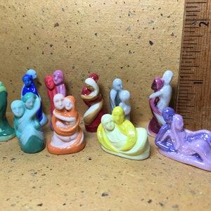 Puede incluir: Una colección de pequeñas figuras de cerámica brillante que representan parejas en diversas poses y colores, incluyendo verde, azul, rosa, naranja, rojo, blanco, amarillo y morado, colocadas junto a una regla de madera de 5 cm.