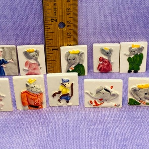 Puede incluir: Una colección de diez pequeñas baldosas de cerámica cuadradas con diseños en relieve de animales antropomórficos. Los animales incluyen elefantes, un mono y un rinoceronte, cada uno con ropa y coronas. Las baldosas son blancas con detalles coloridos.
