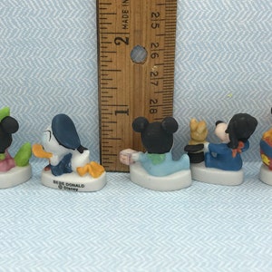 Może przedstawiać: Sześć małych porcelanowych figurek postaci z Disneya, w tym Myszki Miki, Minnie Mouse, Donalda Ducka, Goofy'ego, Pluto i dziecka. Figurki są ubrane w r&oacute;żne stroje i stoją na małych białych podstawkach. Figurki mają około 5 cm wysokości.