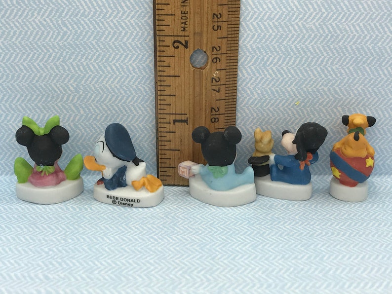 Może przedstawiać: Sześć małych porcelanowych figurek postaci z Disneya, w tym Myszki Miki, Minnie Mouse, Donalda Ducka, Goofy'ego, Pluto i dziecka. Figurki są ubrane w r&oacute;żne stroje i stoją na małych białych podstawkach. Figurki mają około 5 cm wysokości.