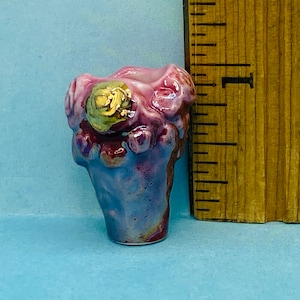 May include: A small, purple and pink ceramic vase with a gold accent. The vase is shaped like a flower and has a textured surface.