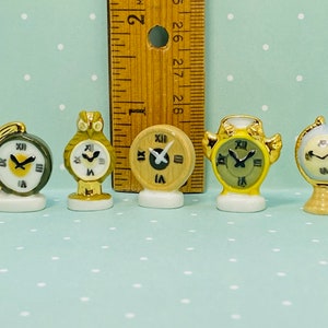 May include: Five miniature porcelain clocks in various styles, including an owl, a globe, and a traditional alarm clock. Each clock features a white face with black Roman numeral markings and black hands.