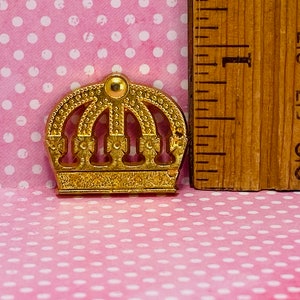 May include: A gold-colored crown with a decorative design. The crown is about 1 inch tall and has a rounded top.