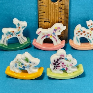 May include: Five miniature ceramic rocking horses with floral designs. The horses are painted white with colorful flowers and leaves. The rocking bases are painted in different colors: green, pink, orange, light green, and light blue.