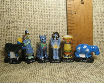 May include: A collection of miniature ceramic figurines, each depicting a different character. The figurines are painted in various colors, including blue, yellow, and black, and are mounted on black bases. The figurines are approximately 1 inch tall.