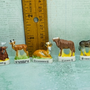 May include: Five miniature ceramic animal figurines, each depicting a different African antelope species. The figurines are painted in realistic colors and feature detailed features. The bases of the figurines are labeled with the French names of the animals: "L'Hippoptrague Noir", "La Gazelle de Grant", "Le Springbok", "Le Gnou", and "L'Oryx Beisa".