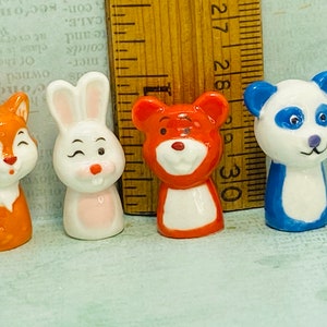 May include: Four small ceramic animal figurines: a fox, a bunny, a bear, and a panda. The fox is orange, the bunny is white, the bear is orange, and the panda is white and blue. Each figurine is approximately 1 inch tall.