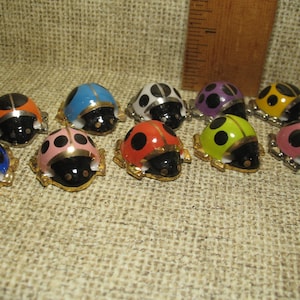 May include: A collection of twelve ladybug figurines, each with a different color and black spots. The ladybugs are made of ceramic and have gold accents.