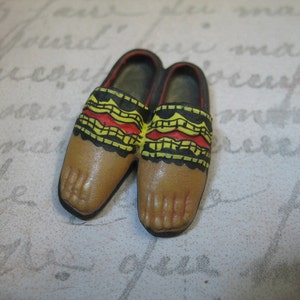 Puede incluir: Dos zapatos de cuero marrón en miniatura con patrones geométricos amarillos, rojos y negros. Los zapatos tienen una punta puntiaguda y una suela plana.