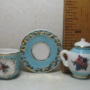 May include: A miniature tea set with a blue and gold floral design. The set includes a teapot, a cup, and a saucer.
