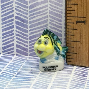 May include: A small ceramic figurine of a yellow and blue fish with a white sailor collar. The figurine is labeled "Polochon &copy; Disney".