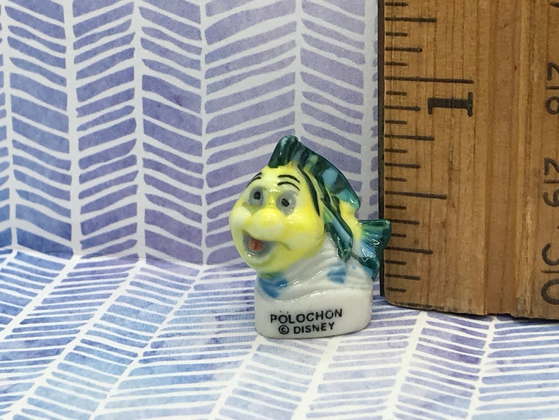 May include: A small ceramic figurine of a yellow and blue fish with a white sailor collar. The figurine is labeled "Polochon &copy; Disney".