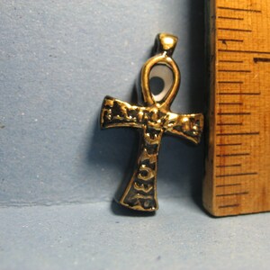 May include: A black and gold ankh pendant with a white center. The ankh is a symbol of life in ancient Egyptian mythology.