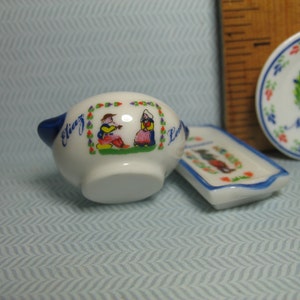 May include: A white ceramic serving dish with blue trim and a colorful illustration of two people in traditional Dutch clothing. The dish has the words "Eliz" and "La" on it.