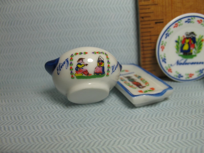 May include: A white ceramic serving dish with blue trim and a colorful illustration of two people in traditional Dutch clothing. The dish has the words "Eliz" and "La" on it.