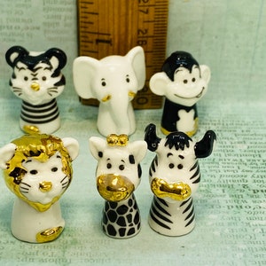 May include: Set of six miniature ceramic animal figurines. The figurines are painted in black and white with gold accents. The animals include a lion, zebra, giraffe, elephant, monkey, and tiger.